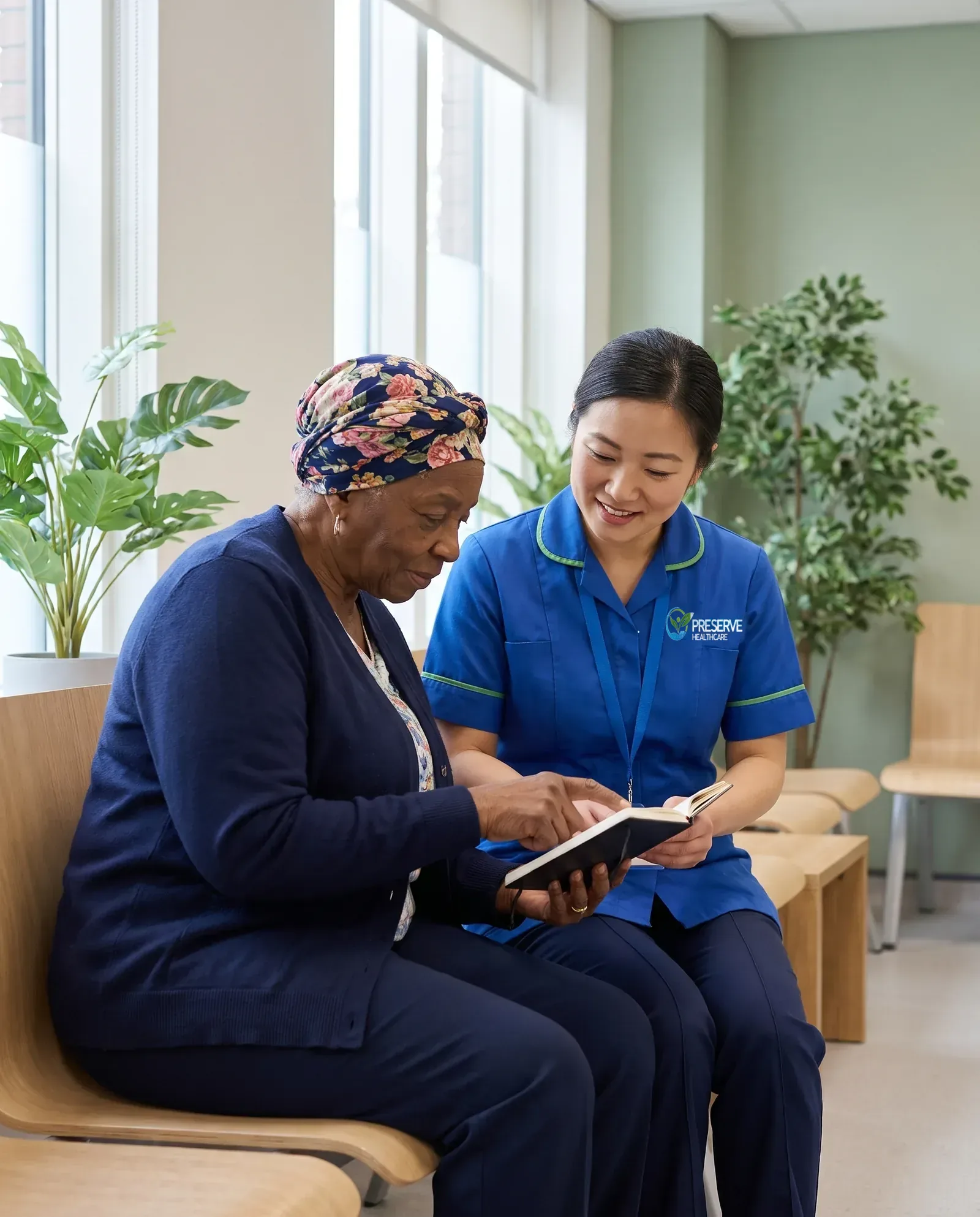 Carer sitting with an elderly woman in a calm waiting area as she prepares questions for her hospital appointment